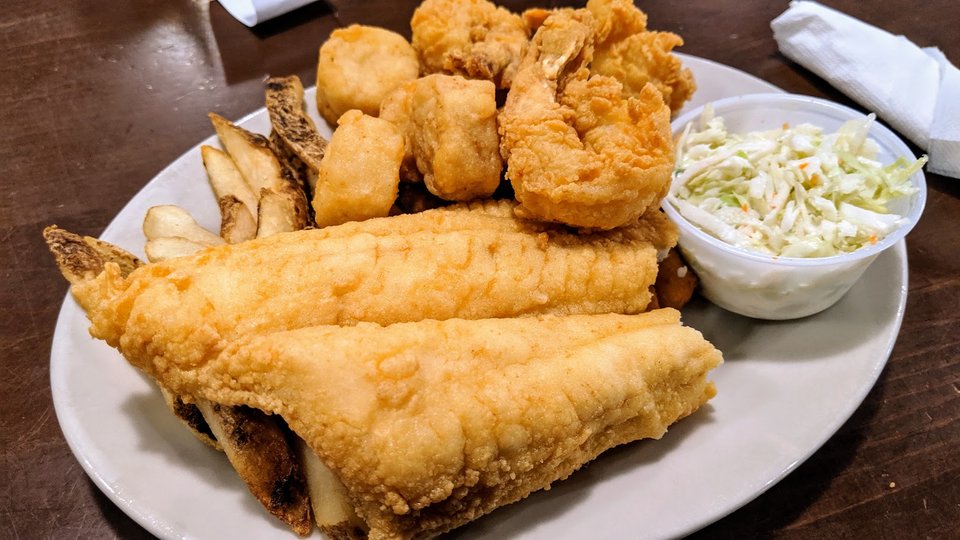 Golden hushpuppies beside seafood platters.